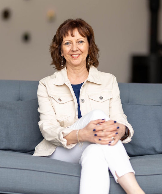 A picture of Gillian Airey Goodwin sitting on a sofa, relaxed and smiling
